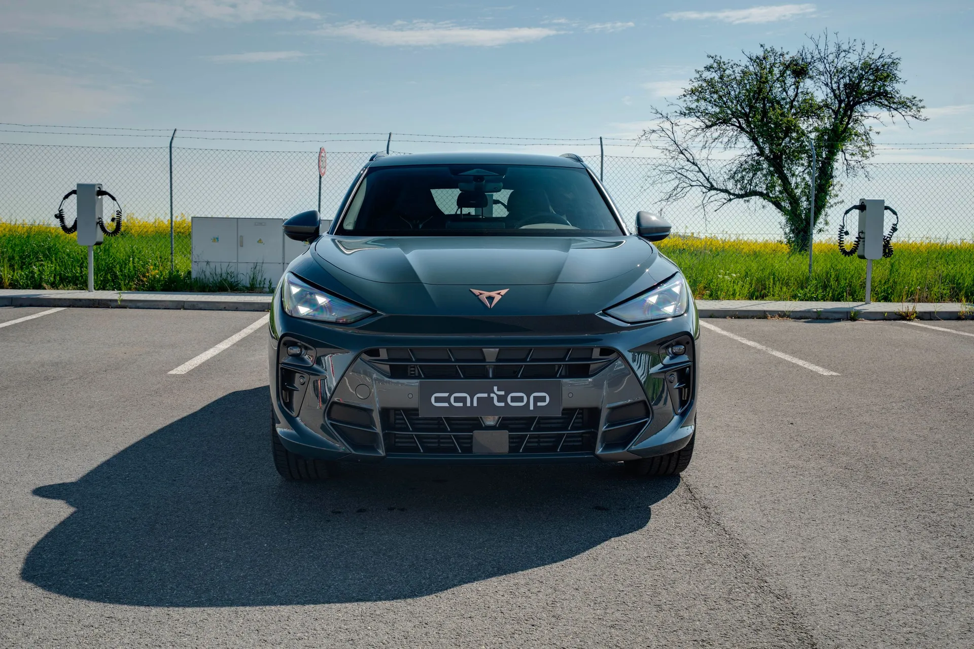 Přední pohled na tmavě šedý Cupra Terramar 1.5 eTSI na parkovišti za slunečného dne