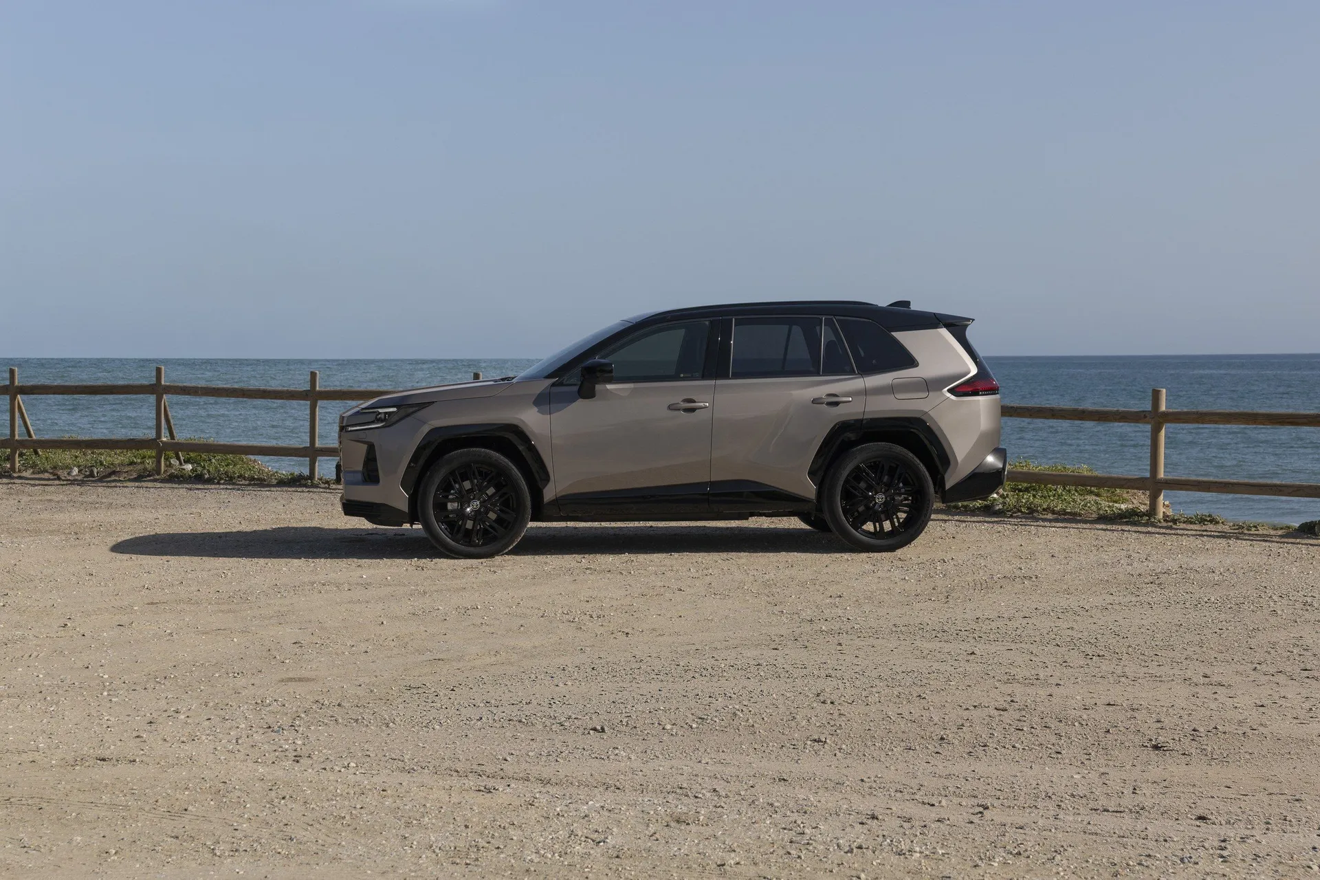 Toyota RAV4 VI 2025 exteriér boční pohled černé ráfky černé okna na pobřeží s dřevěným plotem a modrou oblohou v pozadí