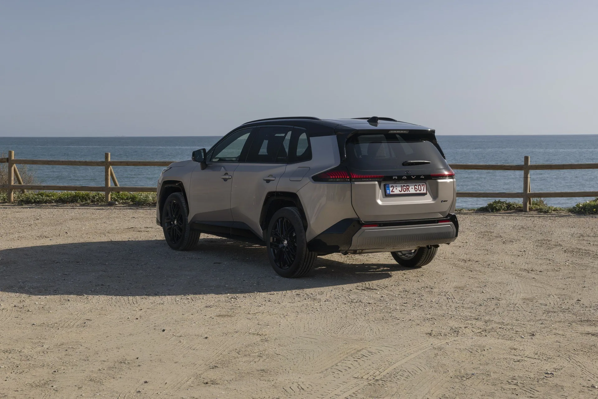 Toyota RAV4 VI 2025 exteriér zadní pohled černé 8 až 9 palcové sportovní disky u moře na pobřeží s majákem a plastovým ochranným pruhem
